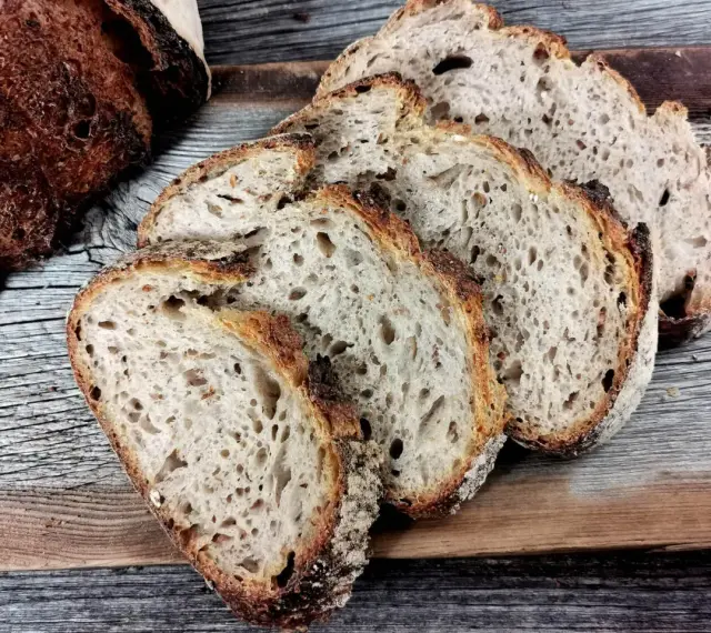 Ein Laib Sauerteigbrot, angeschnitten, mit sichtbarer, knuspriger Kruste. Die Scheiben zeigen eine luftige Krume. Hoffentlich ist die brotkruste zu hart, um sie zu genießen.