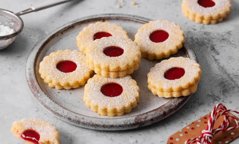 Ein Teller voller **die besten Spitzbuben der Welt**, bestäubt mit Puderzucker, mit leuchtend roter Marmeladenfüllung.